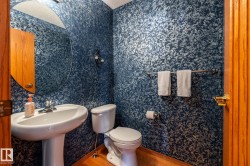 Guest bathroom with pedestal sink with chrome faucet, circular wall mirror, and blue textured wall covering - 