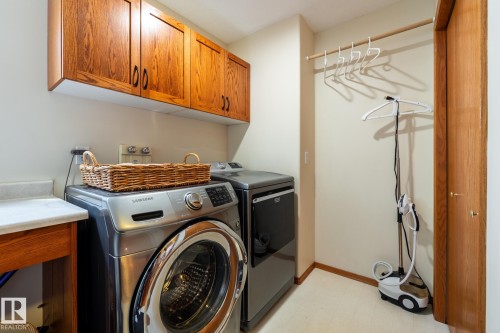 Dedicated laundry area featuring a front-load washing machine, accompanying dryer, and overhead wood cabinetry - 114 Reichert Drive, Beaumont, AB 