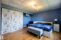 Basement bedroom featuring light wood-finish flooring, a white paneled bed frame with integrated drawers, blue accent walls, and a drop ceiling with recessed lighting - 
