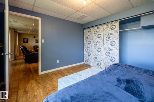Fourth bedroom in the basement featuring a huge window overlooking the back yard and golf course, with wood-finish flooring, a drop ceiling, and a doorway opening into the family room - 114 Reichert Drive, Beaumont, AB 