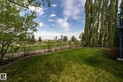 Expansive green lawn with mature trees and a chain-link fence alongside the 14th green - 