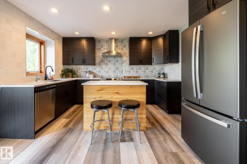 Contemporary kitchen featuring dark wood-finish cabinetry, a light wood-finish island with a white countertop, and patterned tile backsplash - 114 Reichert Drive, Beaumont, AB 