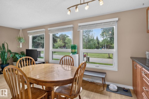 Dining area featuring three large windows with roller blinds, wood-finish flooring, and a kitchen counter with wood cabinetry and a dark countertop - 31 Alpine Boulevard, St. Albert, AB 