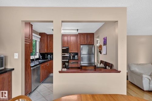 Kitchen featuring wood cabinetry, stainless steel appliances, and a pass-through window with a wood ledge - 31 Alpine Boulevard, St. Albert, AB 