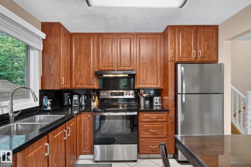 Kitchen featuring wood-finish cabinetry, black countertops, stainless steel appliances, and a double basin sink with a high-arc faucet - 31 Alpine Boulevard, St. Albert, AB 