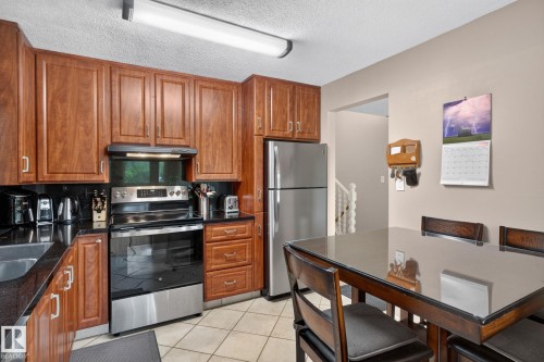 Kitchen featuring wood cabinetry, black countertops, stainless steel appliances, and tile flooring - 31 Alpine Boulevard, St. Albert, AB 