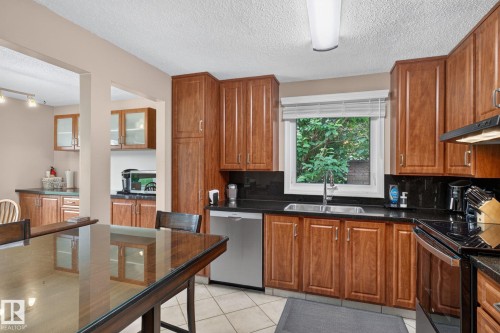 Kitchen featuring wood cabinetry, dark countertops, tile flooring, a stainless steel dishwasher, and a window with blinds - 31 Alpine Boulevard, St. Albert, AB 