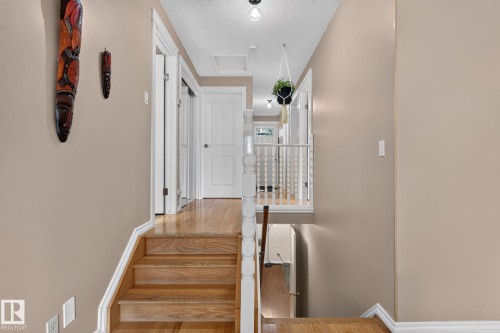 Wood-finish stair treads with white risers and handrail, leading to a hallway featuring wood-finish flooring, white doors, and a ceiling light fixture - 31 Alpine Boulevard, St. Albert, AB 