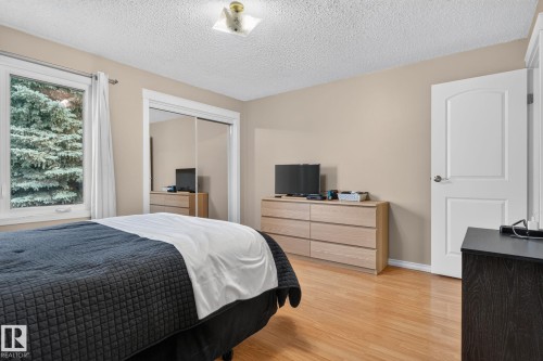 Bedroom featuring wood-finish flooring, a double-paned window, and a mirrored sliding closet door - 31 Alpine Boulevard, St. Albert, AB 