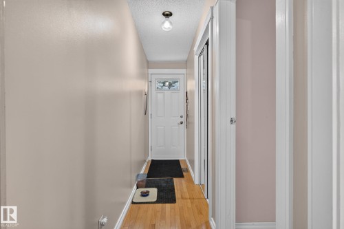 Entryway with wood-finish flooring, a white front door featuring decorative glass, and a built-in closet with mirrored sliding doors - 31 Alpine Boulevard, St. Albert, AB 