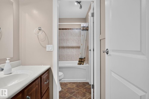 Full bathroom featuring a white vanity with a built-in sink, wood-finish cabinetry, and a shower-over-tub combination with tiled walls - 31 Alpine Boulevard, St. Albert, AB 