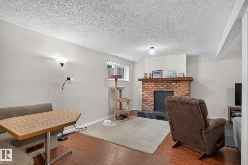 Living area featuring a brick fireplace with a wood mantle, wood-finish flooring, and a window with natural light - 31 Alpine Boulevard, St. Albert, AB 