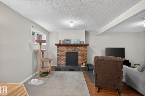 Living area featuring a brick fireplace with a wood mantle, a dark stone hearth, wood-finish flooring, and light-toned walls - 31 Alpine Boulevard, St. Albert, AB 