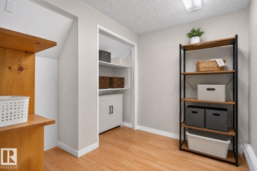 Versatile storage area featuring wood-finish flooring, a built-in shelving unit with white cabinetry and dark hardware, and an additional freestanding shelving unit with metal framing and wood-finish shelves - 31 Alpine Boulevard, St. Albert, AB 