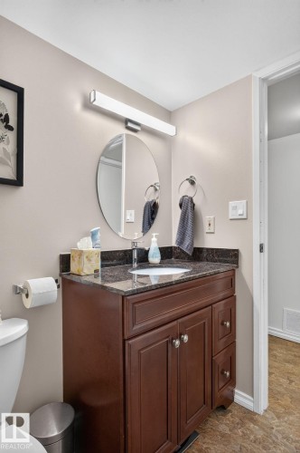 Bathroom featuring a dark wood vanity with a dark speckled countertop, an undermount sink, and a circular mirror - 31 Alpine Boulevard, St. Albert, AB 
