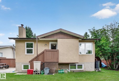 Rear exterior featuring stucco siding, a brown wood-paneled deck with stairs, a visible chimney, and multiple windows - 31 Alpine Boulevard, St. Albert, AB 