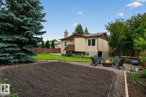 Expansive backyard featuring a central fire pit area with stone surround, a manicured lawn, and a distinct garden plot - 31 Alpine Boulevard, St. Albert, AB 