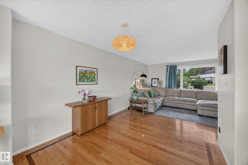 Expansive living area featuring wood-finish flooring with a decorative border, light neutral wall tones, and a woven pendant light fixture - 3411 103 Avenue, Edmonton, AB 