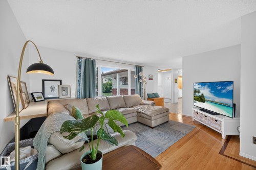 Light-filled living area featuring hardwood flooring, a large window with exterior visibility, a built-in shelf, and recessed lighting - 3411 103 Avenue, Edmonton, AB 