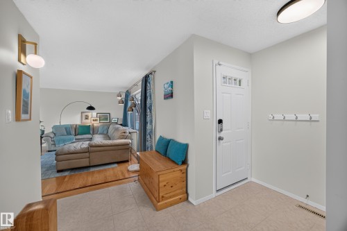 Entryway featuring light-toned tile flooring, a white paneled door with transom windows, and a wall-mounted coat rack - 3411 103 Avenue, Edmonton, AB 