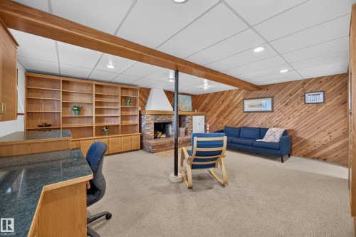 Lower level featuring a brick fireplace with a white hood, wood paneling, and wood beam accents - 3411 103 Avenue, Edmonton, AB 