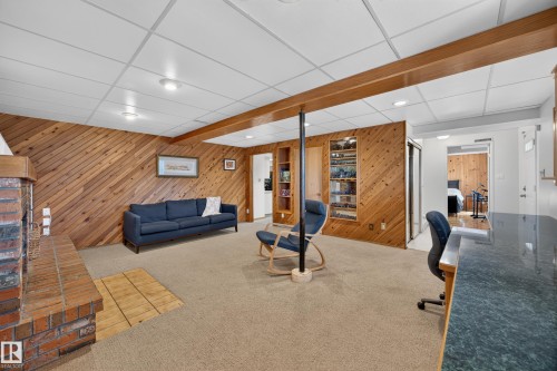 Spacious room featuring wood plank wall paneling, a brick fireplace, dropped ceiling with recessed lighting, built-in shelving, and carpet flooring - 3411 103 Avenue, Edmonton, AB 