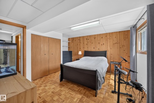 Bedroom featuring wood-finish parquet flooring, wood panel accent wall, recessed lighting, and a large window with privacy blinds - 3411 103 Avenue, Edmonton, AB 