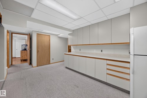 Utility room featuring extensive built-in cabinetry, light-toned countertops, a full-size refrigerator, and textured carpeting - 3411 103 Avenue, Edmonton, AB 