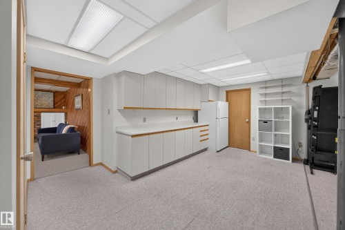 Carpeted room featuring extensive white cabinetry with wood-finish trim, white countertops, and a full-size refrigerator - 3411 103 Avenue, Edmonton, AB 