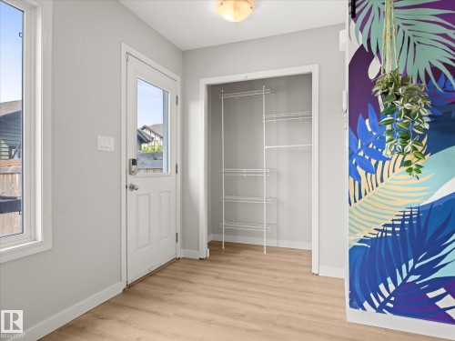 Entryway featuring a glass-paneled door, wood-finish flooring, white trim, a built-in closet with wire shelving, and a decorative wall accent - 473 Orchards Boulevard, Edmonton, AB 
