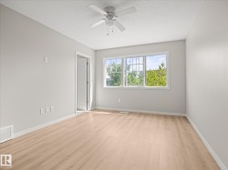 Bright room featuring light-toned wood-finish flooring, a contemporary ceiling fan, and a large multi-pane window - 