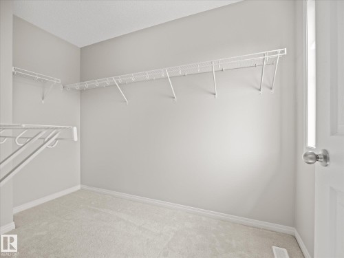 Walk-in closet featuring light gray walls, white wire shelving, light-colored carpeting, and a white paneled door with a brushed nickel knob - 473 Orchards Boulevard, Edmonton, AB 