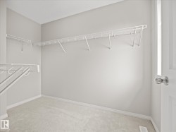 Walk-in closet featuring light gray walls, white wire shelving, light-colored carpeting, and a white paneled door with a brushed nickel knob - 