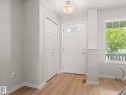 Entryway featuring wood-finish flooring, a white paneled front door with decorative glass inserts, and a double-door closet with louvered panels - 473 Orchards Boulevard, Edmonton, AB 