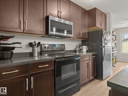 Kitchen featuring dark wood-finish cabinetry with brushed metal hardware, dark countertops, and stainless steel appliances including a refrigerator, microwave, and electric range - 