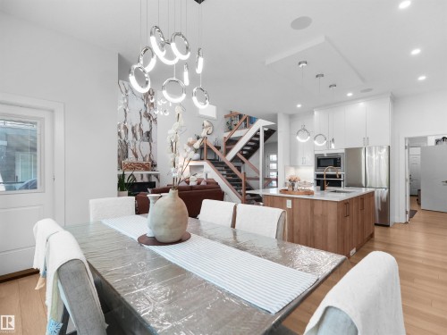 Open-concept interior featuring wood-finish flooring, a contemporary chandelier, recessed lighting, and a modern kitchen with stainless steel appliances and an island - 320 38 Street, Edmonton, AB 