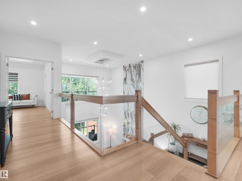 Upper landing featuring wood-finish flooring, glass panel railings with wood handrails, recessed ceiling lighting, and a contemporary chandelier - 320 38 Street, Edmonton, AB 