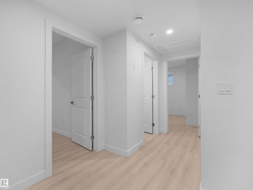 Hallway featuring light wood-finish flooring, white walls, recessed ceiling lighting, and multiple paneled doors - 320 38 Street, Edmonton, AB 