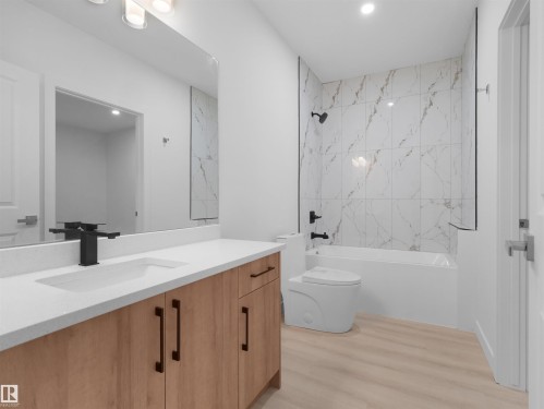 Bathroom featuring a light wood-finish vanity with a white countertop and integrated sink, matte black faucet, and a large wall-mounted mirror - 320 38 Street, Edmonton, AB 