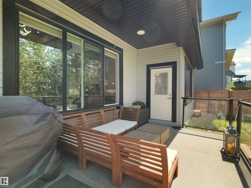 Covered outdoor patio with a concrete surface, featuring a glass panel railing, a single white exterior door, and large sliding glass doors - 320 38 Street, Edmonton, AB 