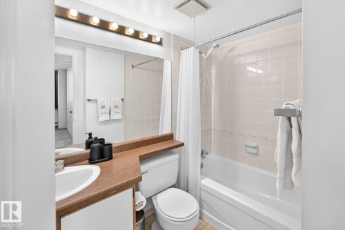 Bathroom featuring a vanity with an integrated sink, a large wall-mounted mirror, a full bathtub with a shower, and light-toned wall tiling - 806 10545 Saskatchewan Drive, Edmonton, AB 