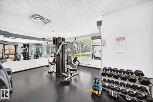Dedicated fitness area featuring dark flooring, mirrored walls, ample natural light, and a multi-station weight machine - 806 10545 Saskatchewan Drive, Edmonton, AB 