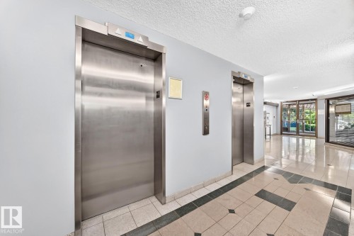 Lobby featuring twin stainless steel elevators, patterned tile flooring with dark accent borders, and extensive glass doors opening to exterior landscaping - 806 10545 Saskatchewan Drive, Edmonton, AB 