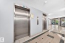 Lobby featuring twin stainless steel elevators, patterned tile flooring with dark accent borders, and extensive glass doors opening to exterior landscaping - 806 10545 Saskatchewan Drive, Edmonton, AB 