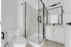 Bathroom featuring a glass-enclosed shower with tiled walls, a white vanity with gold-tone hardware, a rectangular framed mirror, and light wood-finish flooring - 