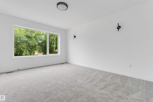 Spacious room featuring a large window, gray carpet, white walls, black wall sconces, and a flush mount ceiling fixture - 3605 112 Ave, Edmonton, AB 