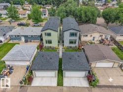 Twin modern homes featuring light green and light grey facades, each with a dedicated detached garage - 
