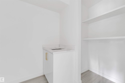 Compact wet bar featuring a white cabinet with gold-toned hardware, an integrated sink, and a stone-finish countertop - 3605 112 Ave, Edmonton, AB 