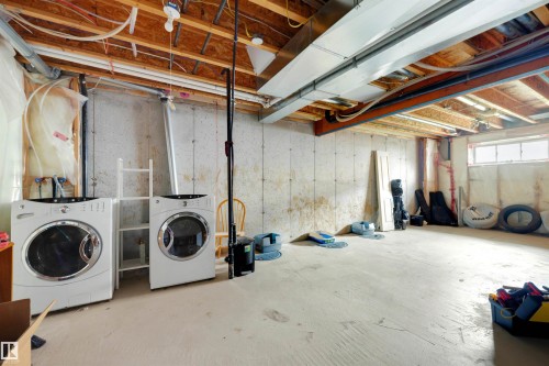 Unfinished basement space featuring concrete walls and flooring, exposed ceiling joists, and a utility area with hookups for laundry appliances - #28 290 Spruce Ridge Rd, Spruce Grove, AB - Indoor