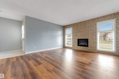 Spacious interior room featuring wood-finish flooring, a decorative accent wall with an inset fireplace, and two large windows providing natural light - 193 Woodvale Road W, Edmonton, AB 